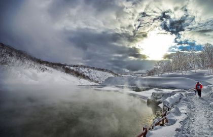 寒冷的冬天大雪后的深山里湖水热气弥漫小路上一人穿红色羽绒服的背影