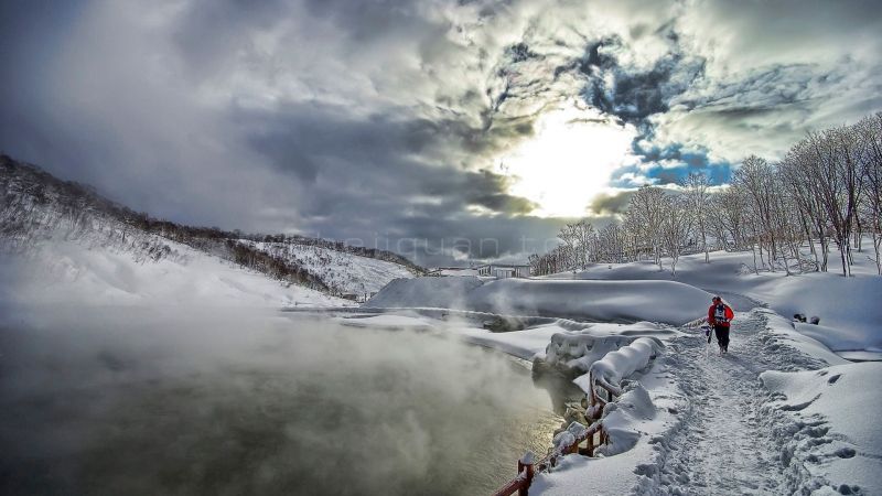 寒冷的冬天大雪后的深山里湖水热气弥漫小路上一人穿红色羽绒服的背影